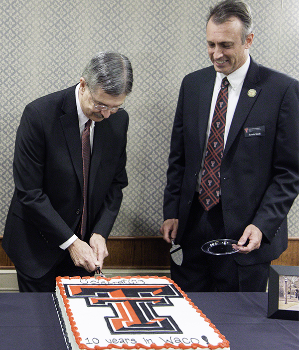 Lewis Snell and Michael Galyean stand over a cake with the Texas Tech logo as it rests on a table 