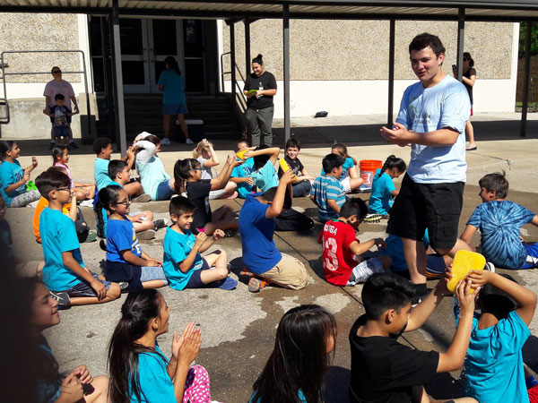 A Charitable Crusaders volunteer directs local students at an elementary school on an activity for field day.