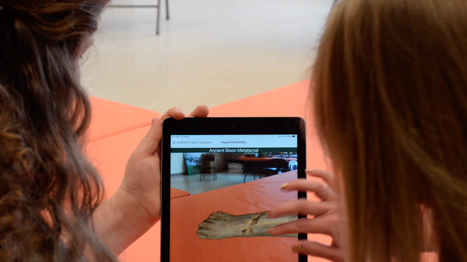 two people touching an ipad screen to rotate a bison bone in augmented reality