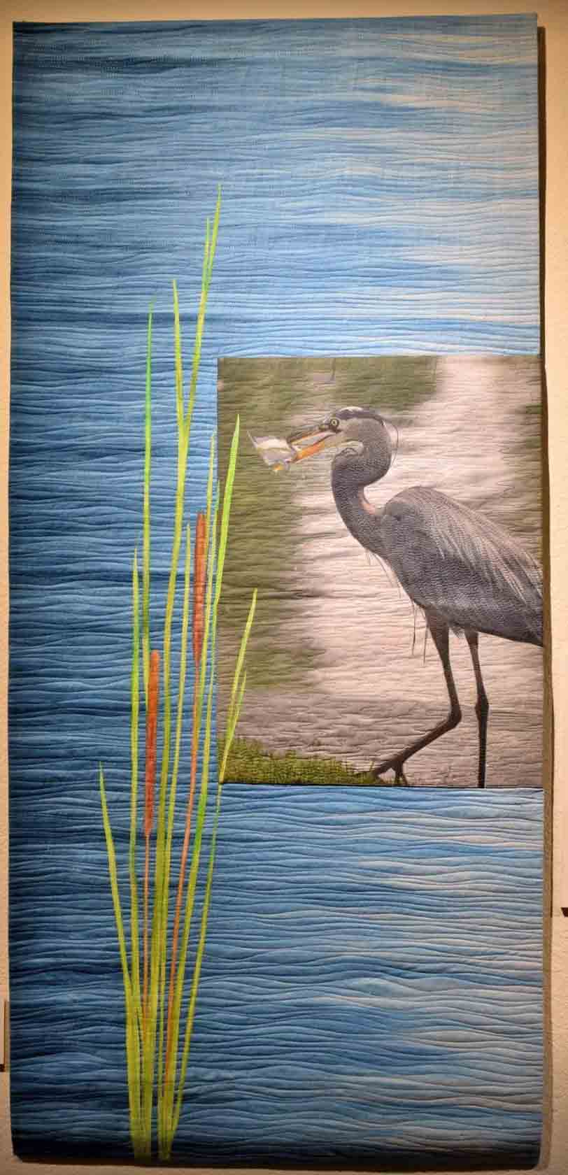 vertically oriented art quilt with water catails plant and heron