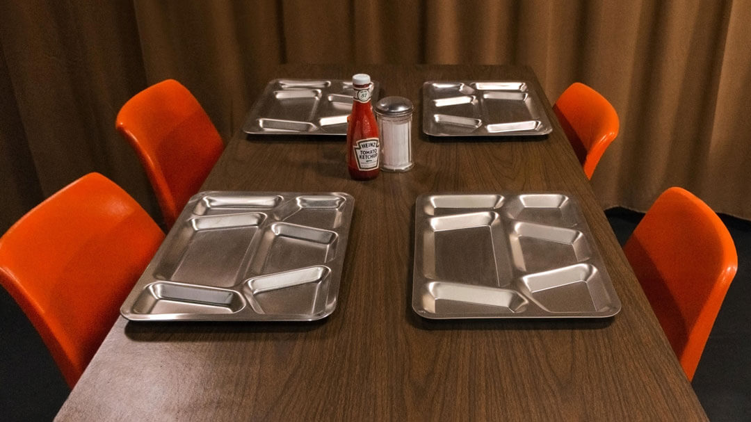 A table with four empty, metal food trays arranged neatly.