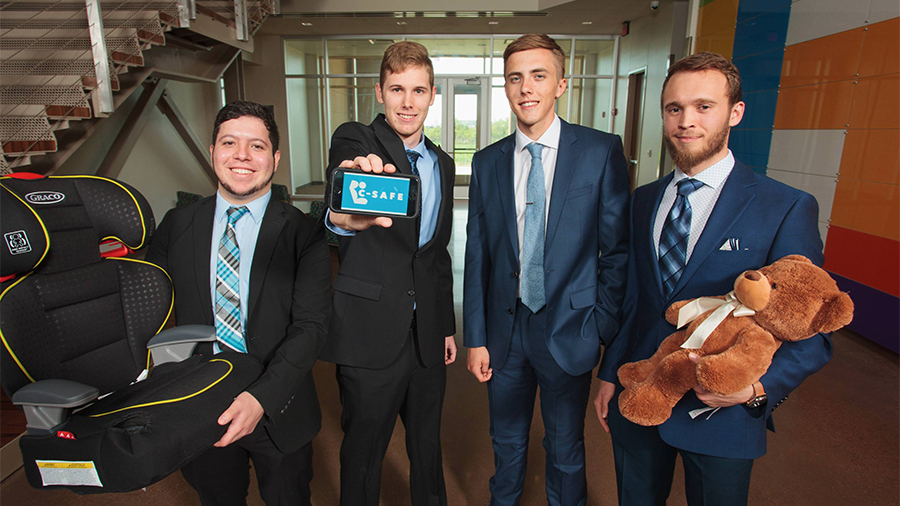 four men in suits. one on left holding a carseat with prototype. one on right holding teddy bear
