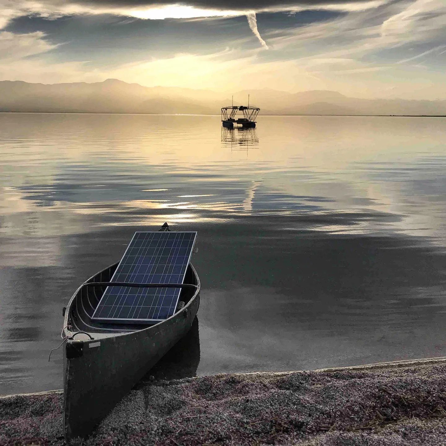 A boat carrying a solar panel docked on the shore. Another boat is floating towards the horizon.