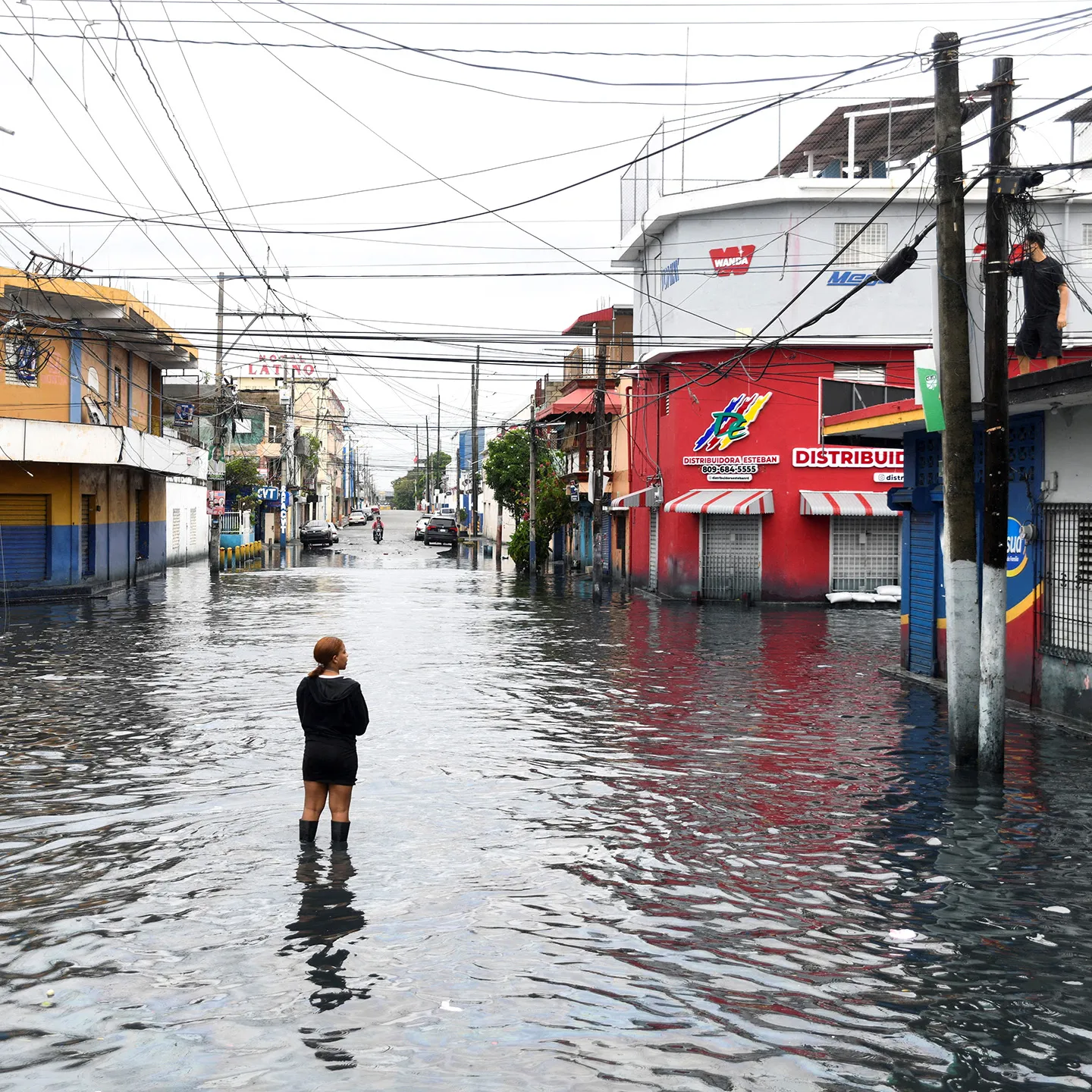 Photo of Santo Domingo flooded. A person is standing in the middle of a flooded street.