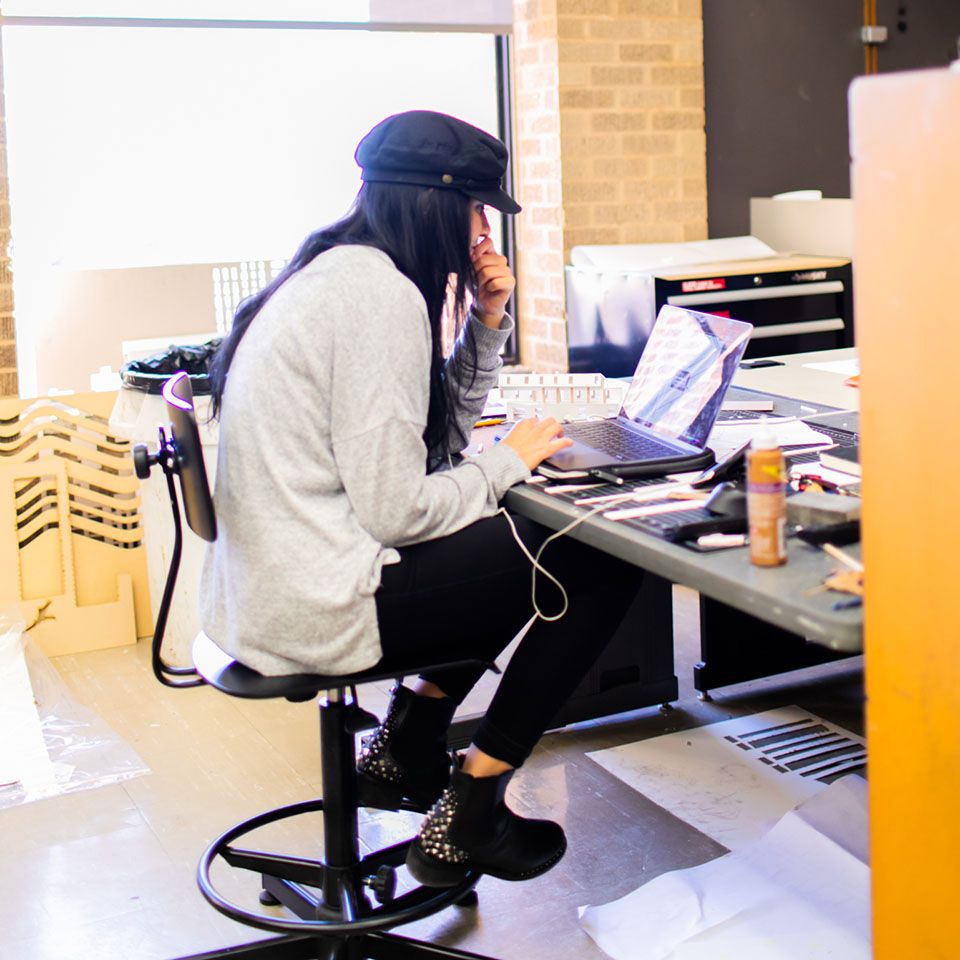 Student working in studio space with laptop and materials on desk.