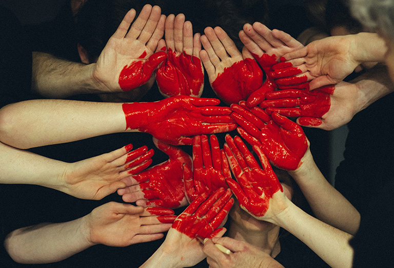 hands grouped together with a red heart painted on them