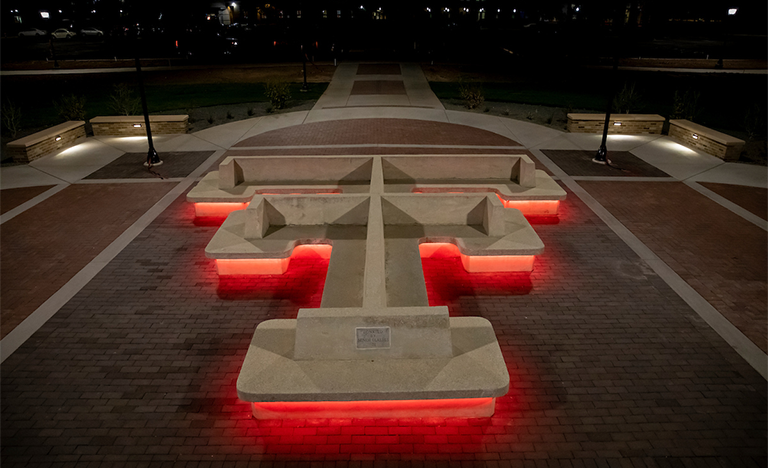 park bench with red lights illuminating under it. the bench is in the shape of texas tech double t