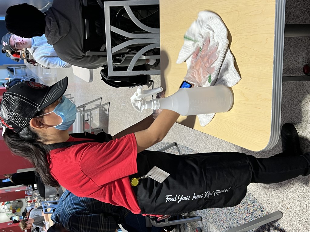 Student cleaning tables in a commercial restaurant setting