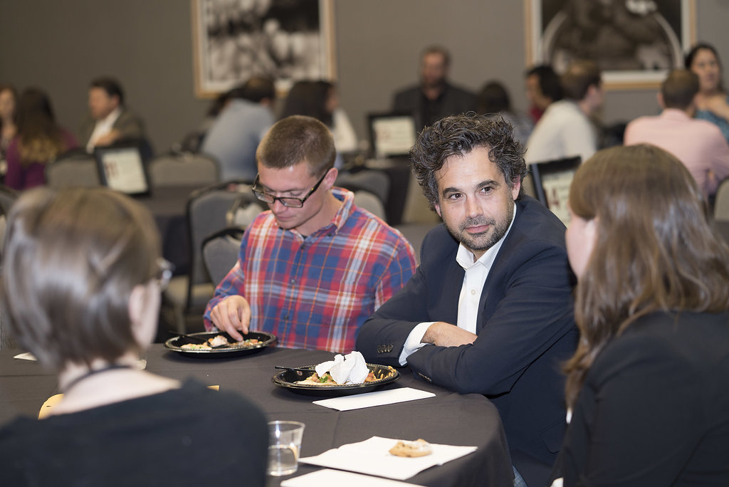 A faculty member discusses their work with students over lunch