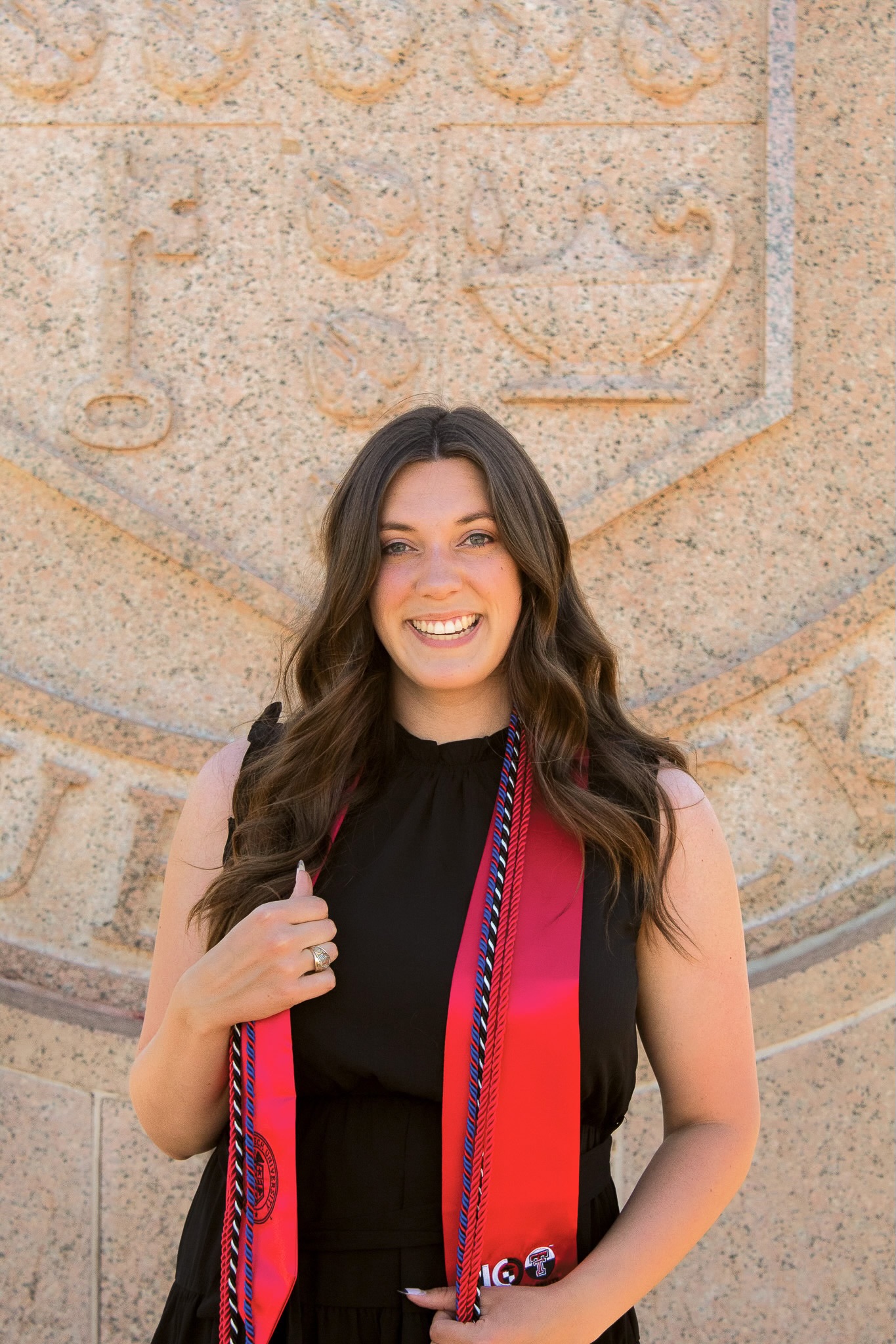 Woman wearing black dress and graduation cords in front of Texas Tech seal