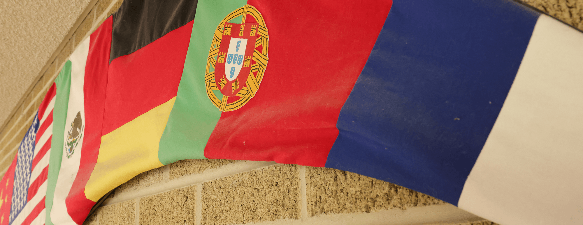 multiple country flags made into a banner that sits against a brick wall in the cmll building