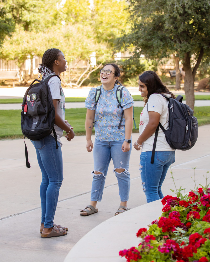 Three students with backpacks chat outdoors at the Texas Tech campus.