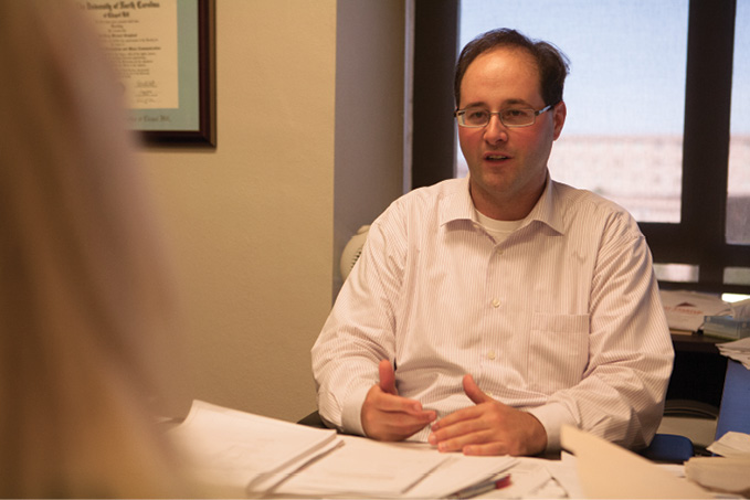 Dr. Geoffrey Graybeal sitting at a desk speaking with a student