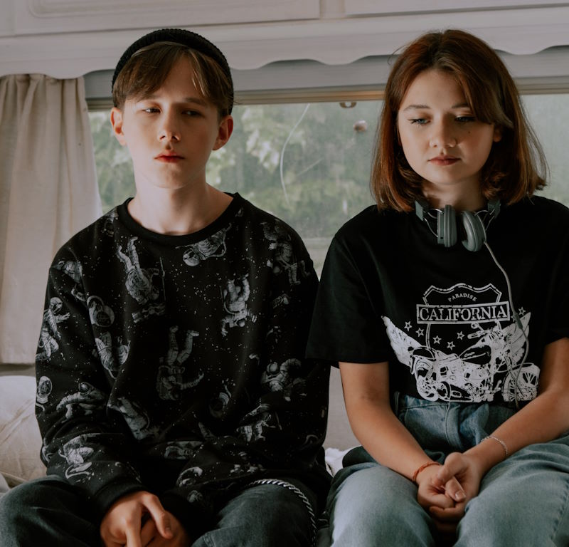 two adolescents sitting side by side on a bed