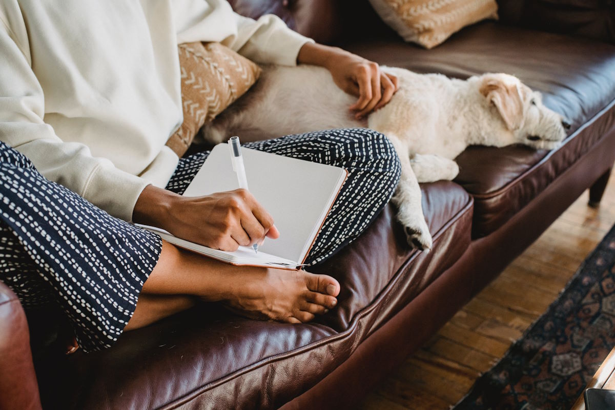 woman sitting on couch with a journal and a dog