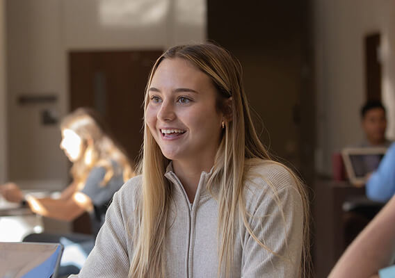 student sitting a a table looking off the side smiling