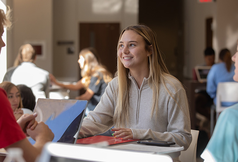 student sitting a a table looking off the side smiling
