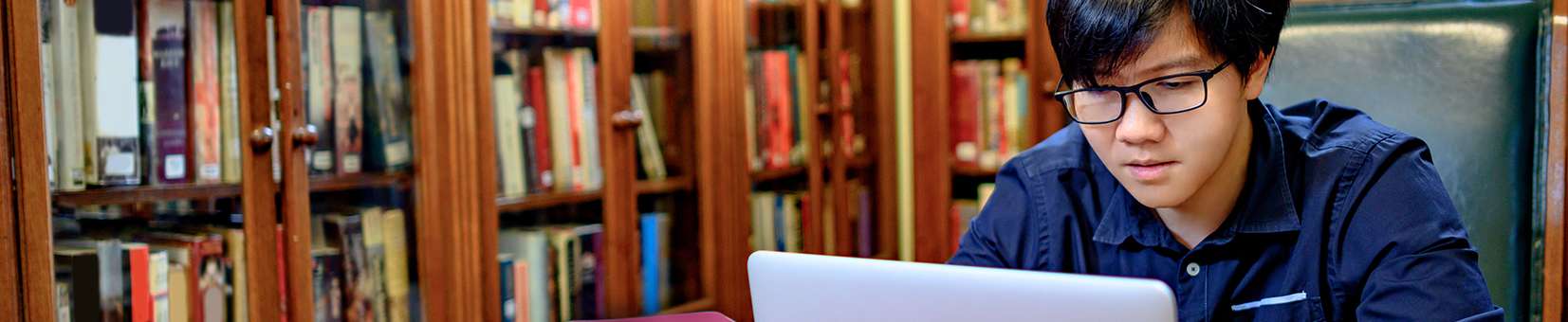 Photo of a student in a library on a laptop