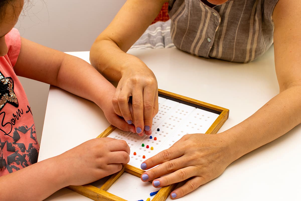 Closeup of teacher and student hands learning Braille on a board with movable pegs.