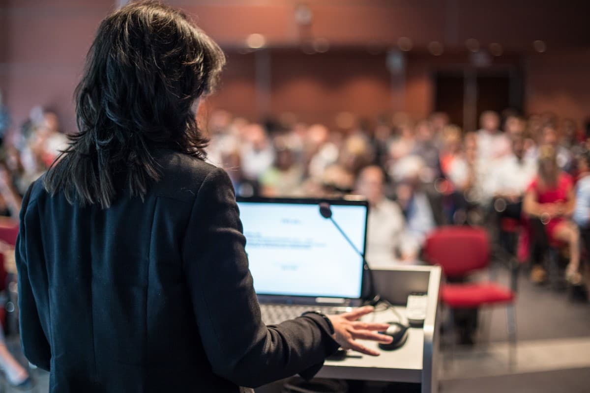 Speaker at a conference giving a presentation in front of an auditorium of listeners.