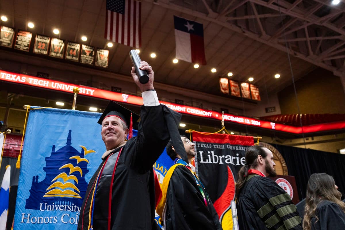 TTU graduate holding diploma aloft.