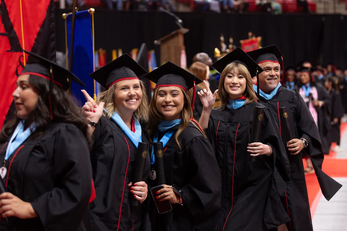 A group of Texas Tech graduates smiling and giving the guns up sign at graduation.