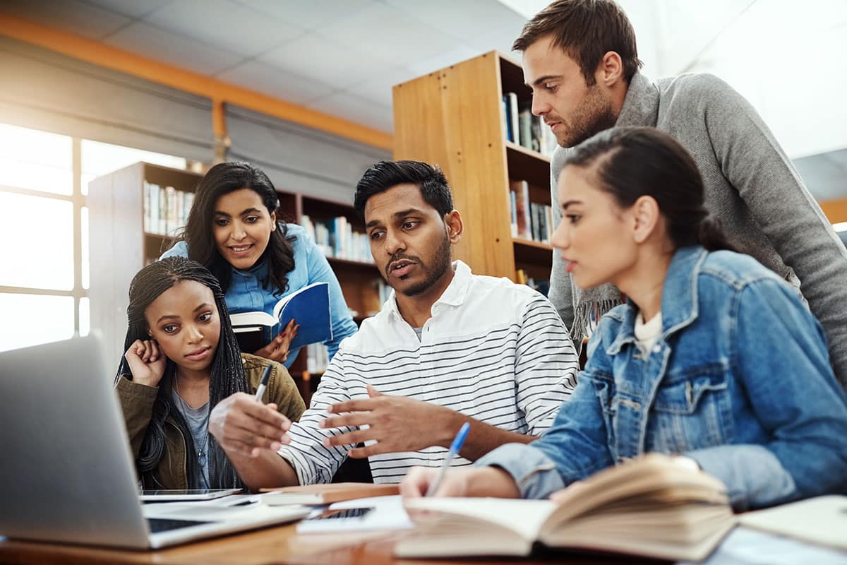 Group of students in a library around a laptop