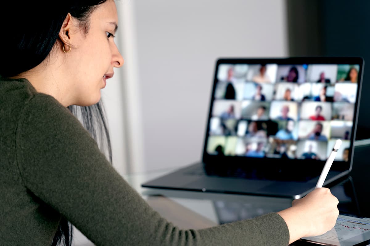 Woman attends class via virtual meeting and takes notes with tablet.
