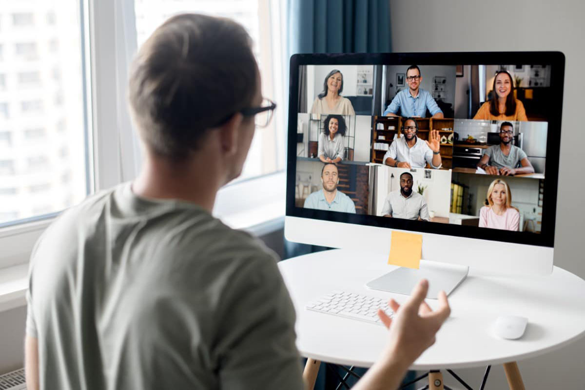 Man on computer in an online meeting with a gallery of other attendees on his screen.
