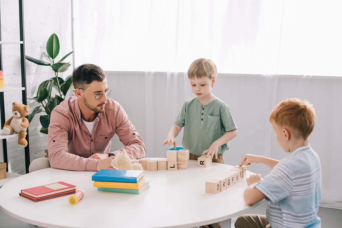 Teacher and two students with wooden letter blocks.