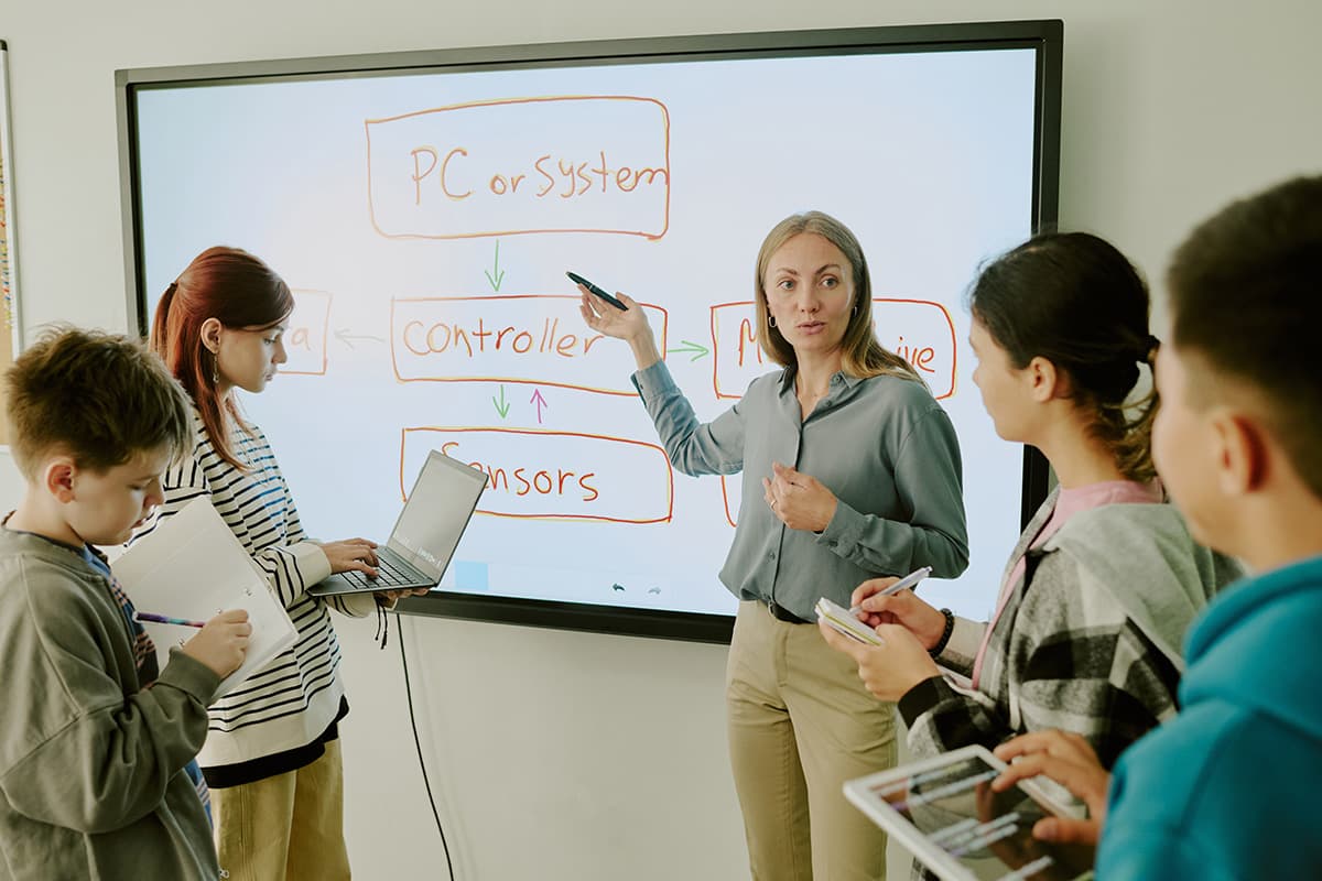 Teacher at digital whiteboard explaining lesson to high school robotics class