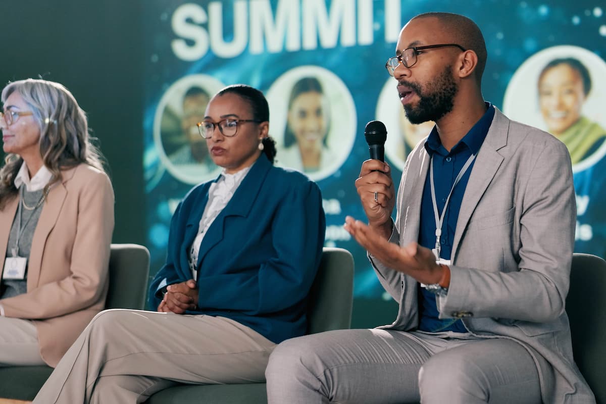Three speakers on a conference presentation stage for a panel discussion.