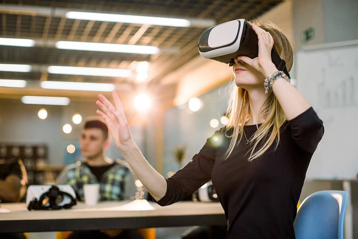 Woman using VR goggles with colleagues in background.