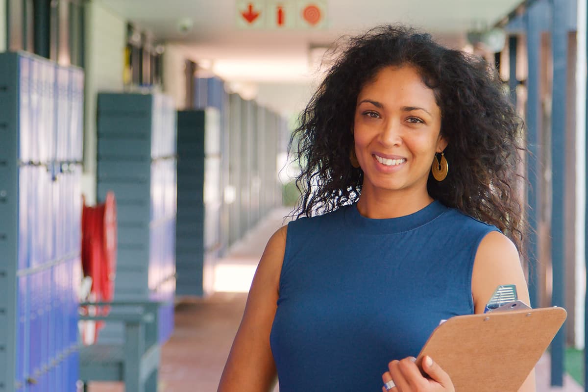 Woman holding clipboard in high school hallway.