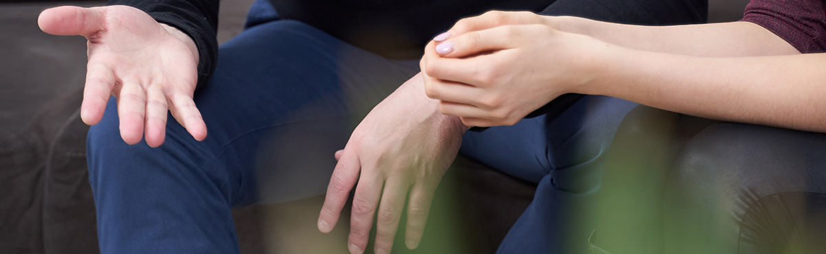 Banner image - close up photo of the hands of a man and woman, seated, in conversation