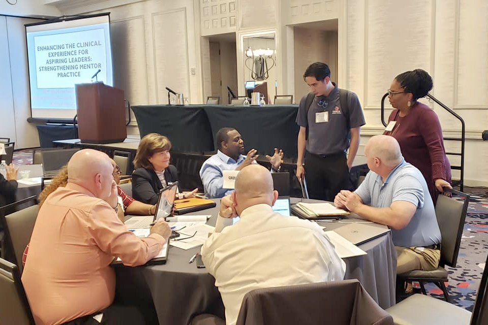 Principal Fellow Kyle Noda standing near a table of educators, talking to them