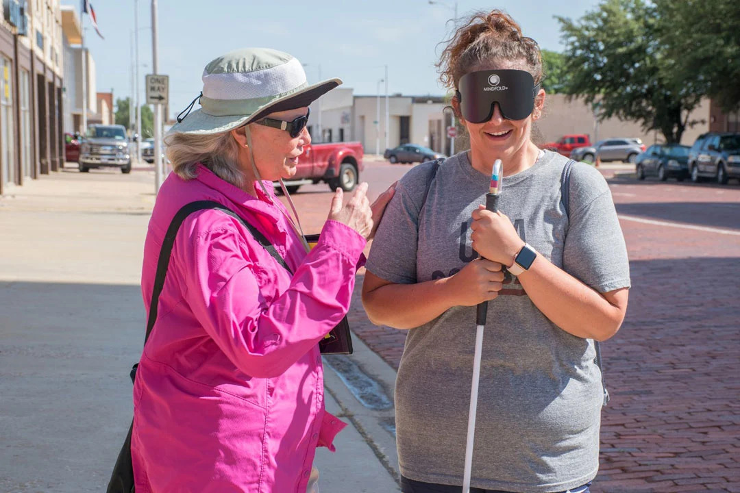 Photo of Dr. Nora Griffin-Shirley instructing a blindfolded person with a white cane on how to navigate an intersection in downtown Lubbock.