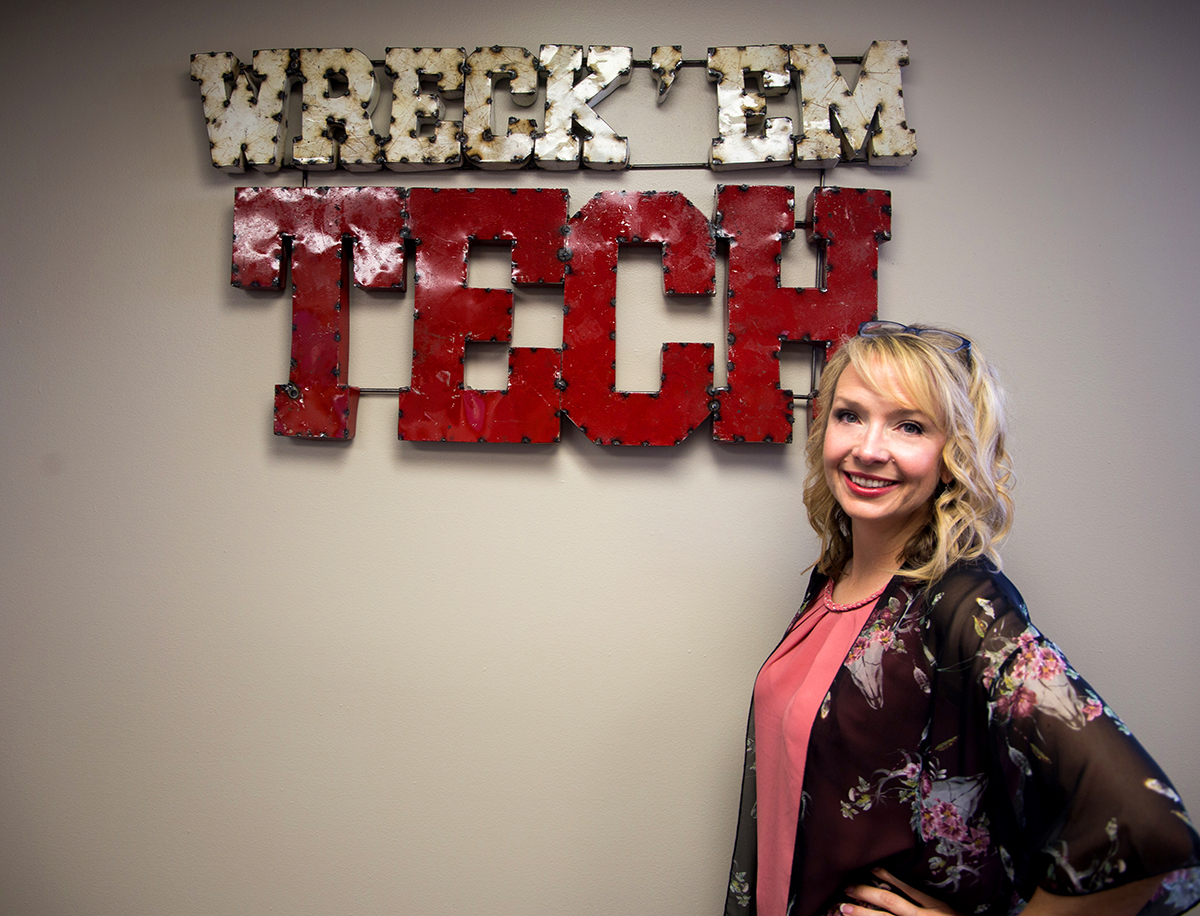 Jessica Thomas stands next to wall art that reads "Wreck' em Tech" and smiles with both hands on her hips