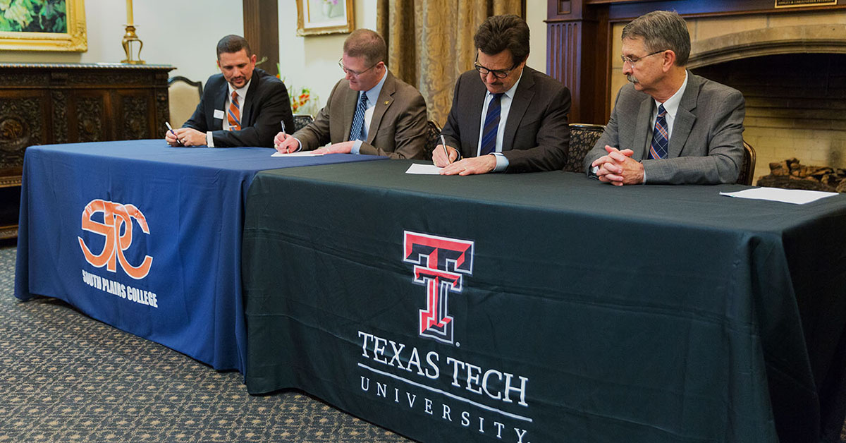 Representatives from South Plains College and Texas Tech University sit at adjacent tables and sign documents