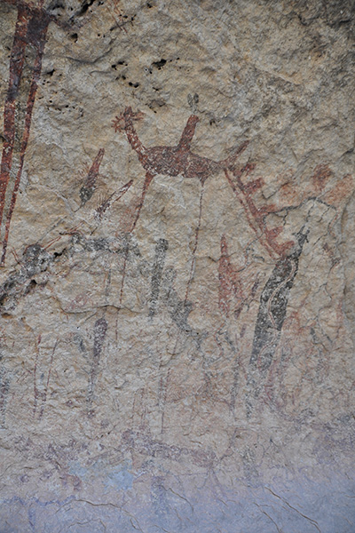 A cave drawing on brown rock that displays what appears to be a large animal towering over other smaller animals.