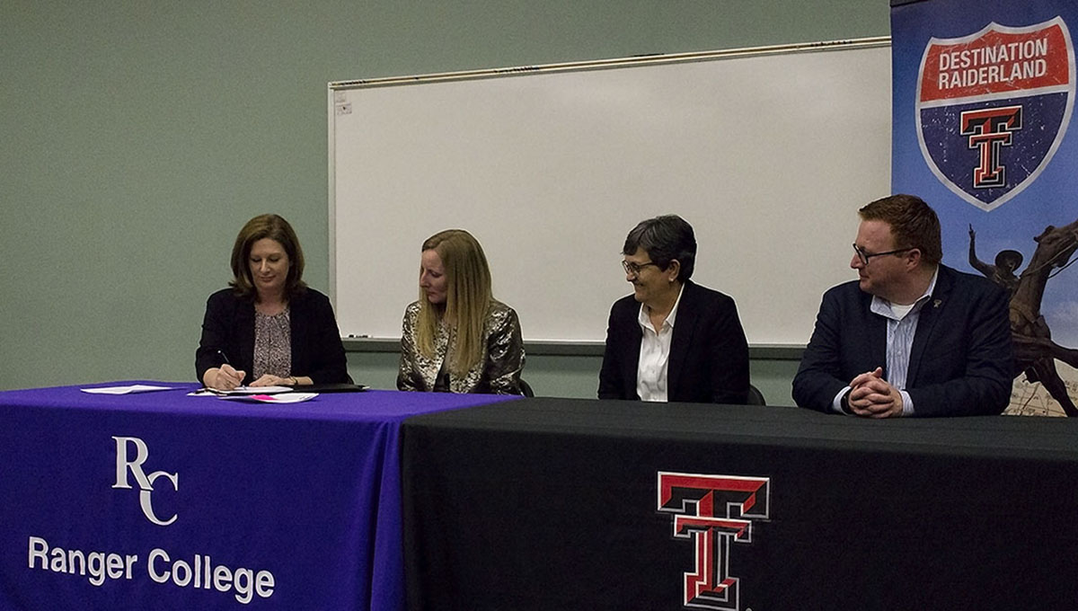 Representatives of elearning & academic partnerships and ranger college sit side-by-side behind two long rectangular tables draped with each college's logo