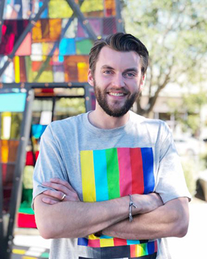 Timoth Howard facing the camera and smiling while standing outside near a multi-colored structure.