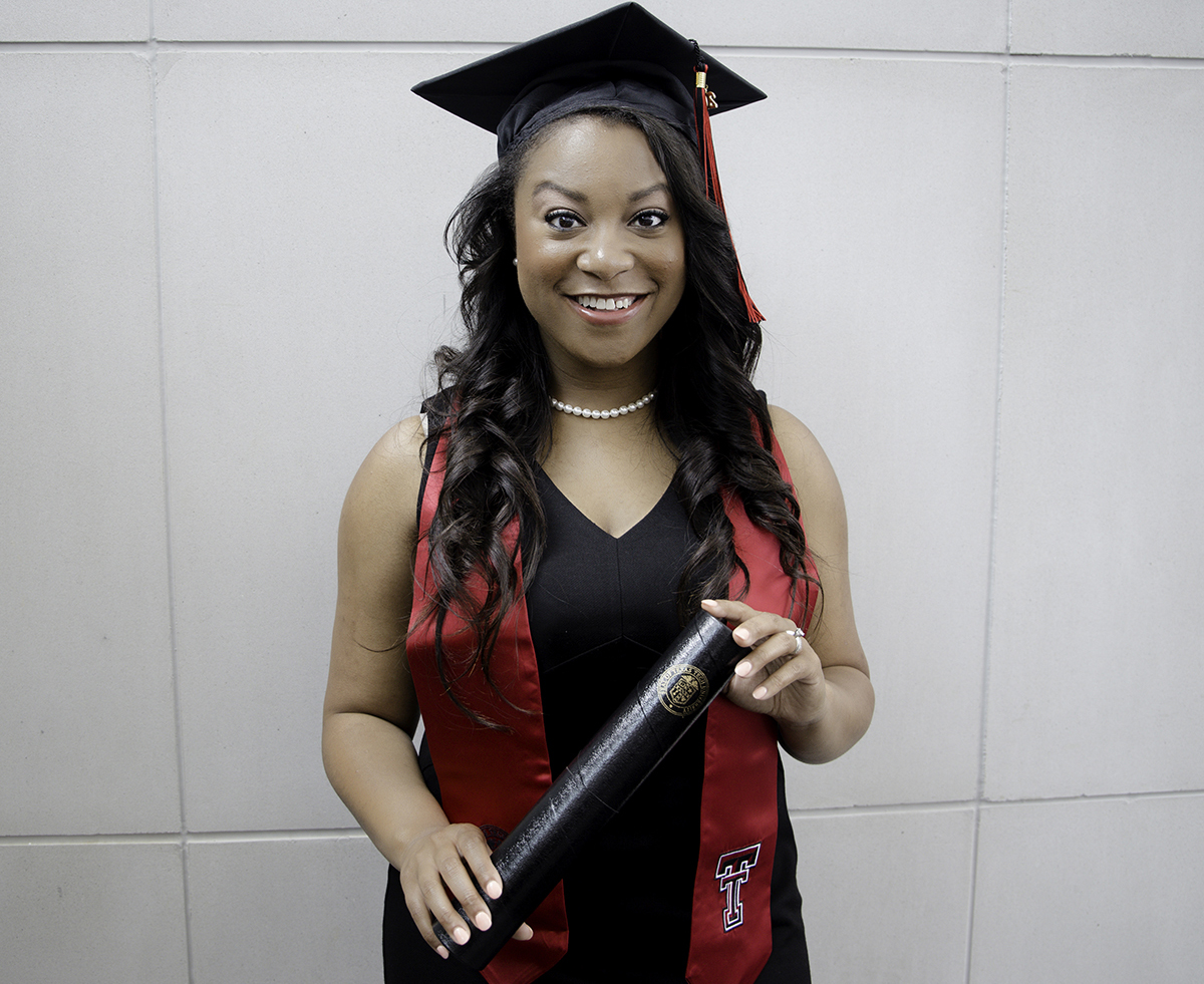 A young woman wearing a black graduation cap, black dress and red texas tech stole holds a black casing for her diploma while smiling at the camera 