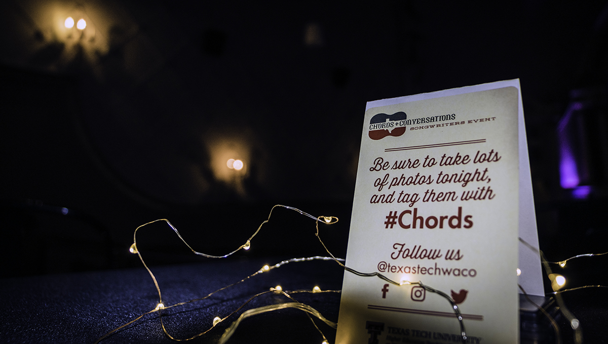 A tent card rests on a blue carpeted floor with the chords and conversations logo and the words "Be sure to take lots of photos tonight, and tag them with #Chords"