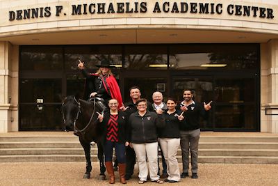 Texas Tech at Waco staff, the Masked Rider and Fearless Champion stand on the steps in front of the Dennis F. Michaelis Academic Center