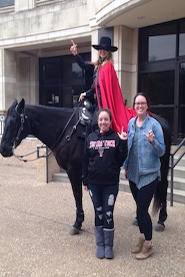 The Masked Rider sits on top of Fearless Champion who is standing behind two a Texas Tech students.