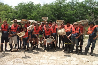 A group of students standing closely while wearing orange life preservers and holding nets.