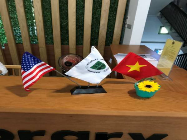 A brown office desk with decor of the American Flag, St. Nicholas flag and the Vietnam Flag held together by a flag holder.
