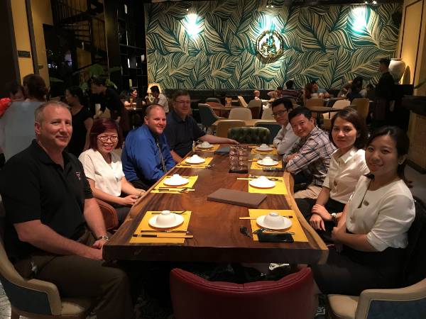 TTU K-12 and St. Nicholas personnel face the camera while sitting on both sides of a table at a restaurant in Vietnam.
