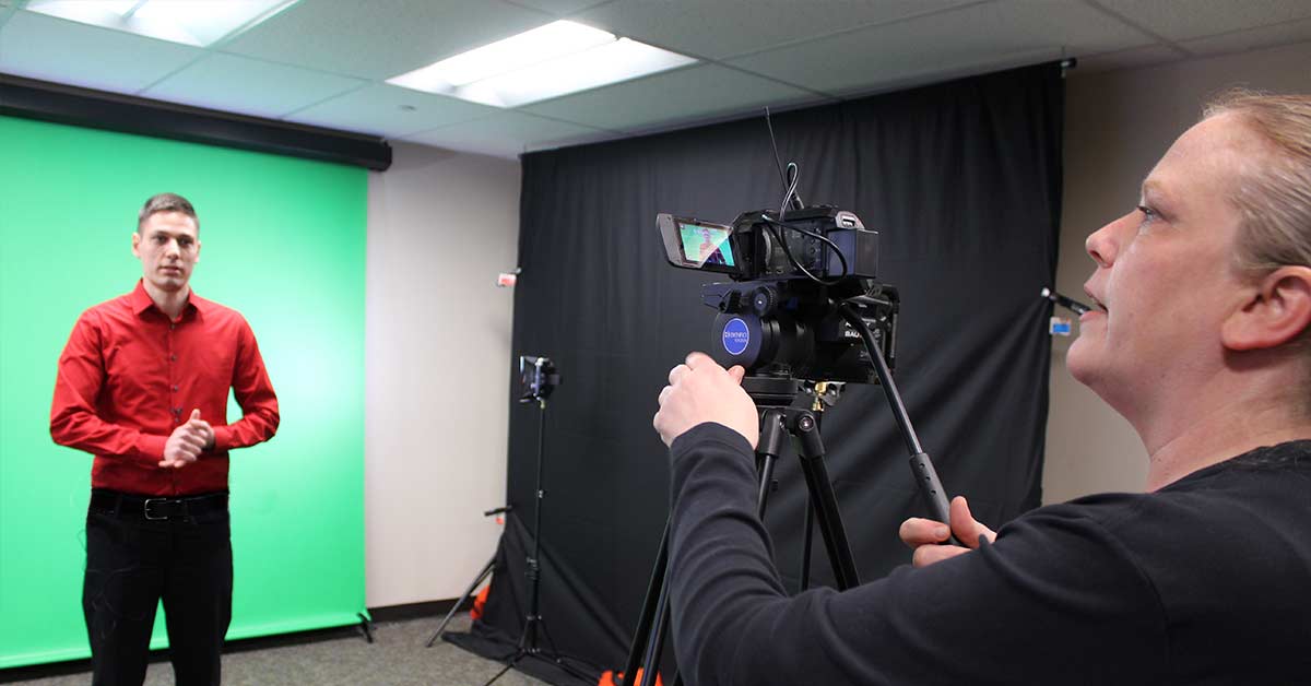 Graphic of a man in a red shirt standing in front of a green screen as a woman behind a camera records him.